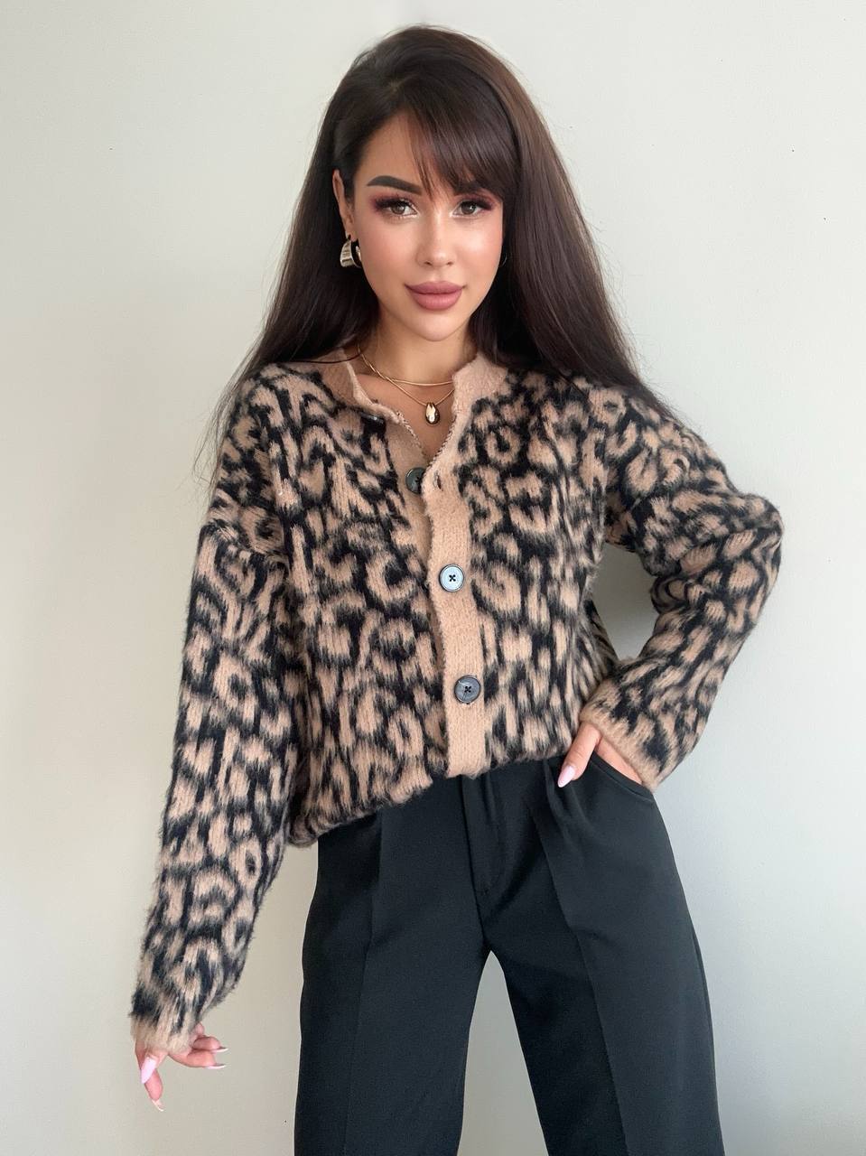 Woman wearing a leopard print cardigan over a beige top with black pants against a plain background