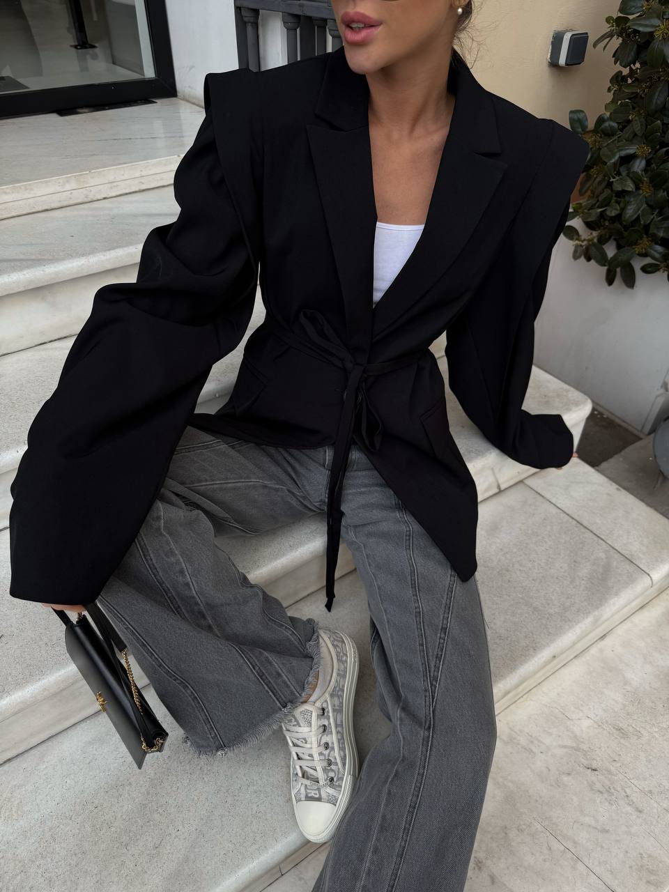 Person wearing a black blazer, white top, and gray pants sitting on steps.