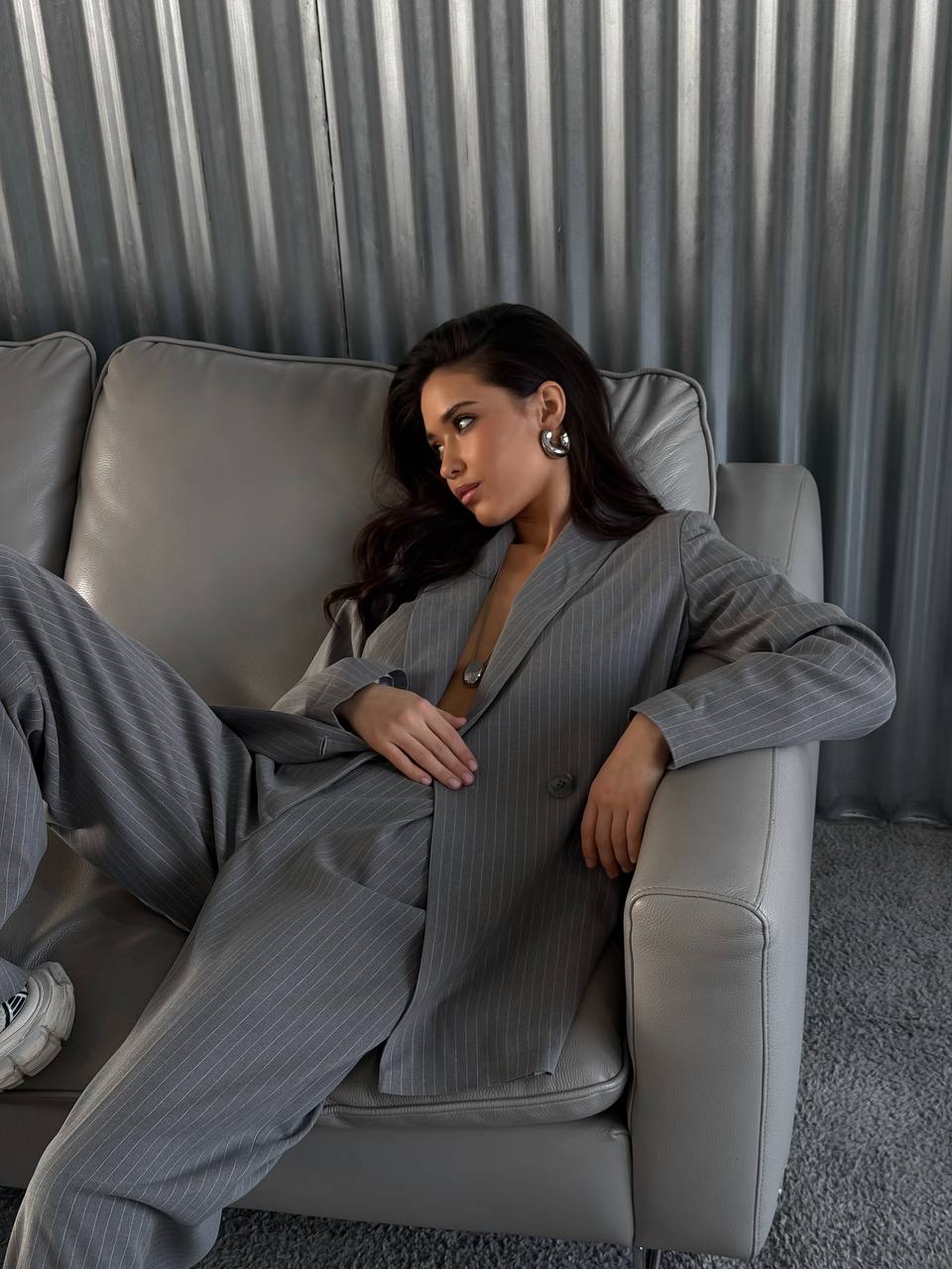 Woman in a gray suit sitting on a gray couch with a neutral background