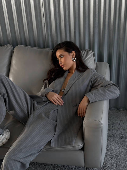 Woman in a gray suit sitting on a gray couch with a neutral background