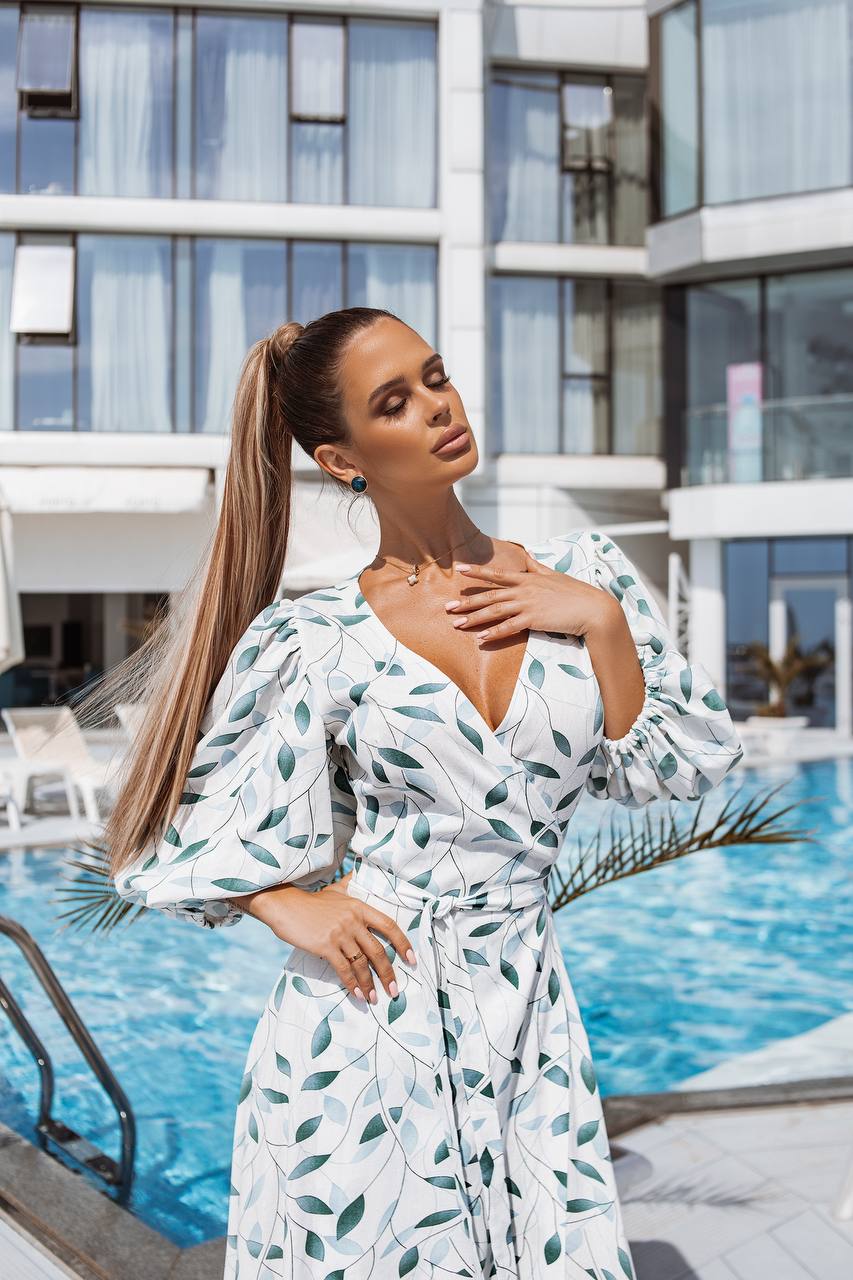 Woman in a white dress with green leaf pattern by a poolside.