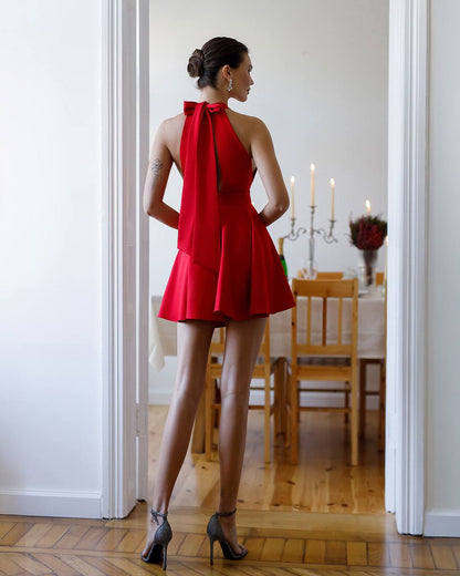 Woman in a red dress standing in a room with wooden flooring and a dining table.