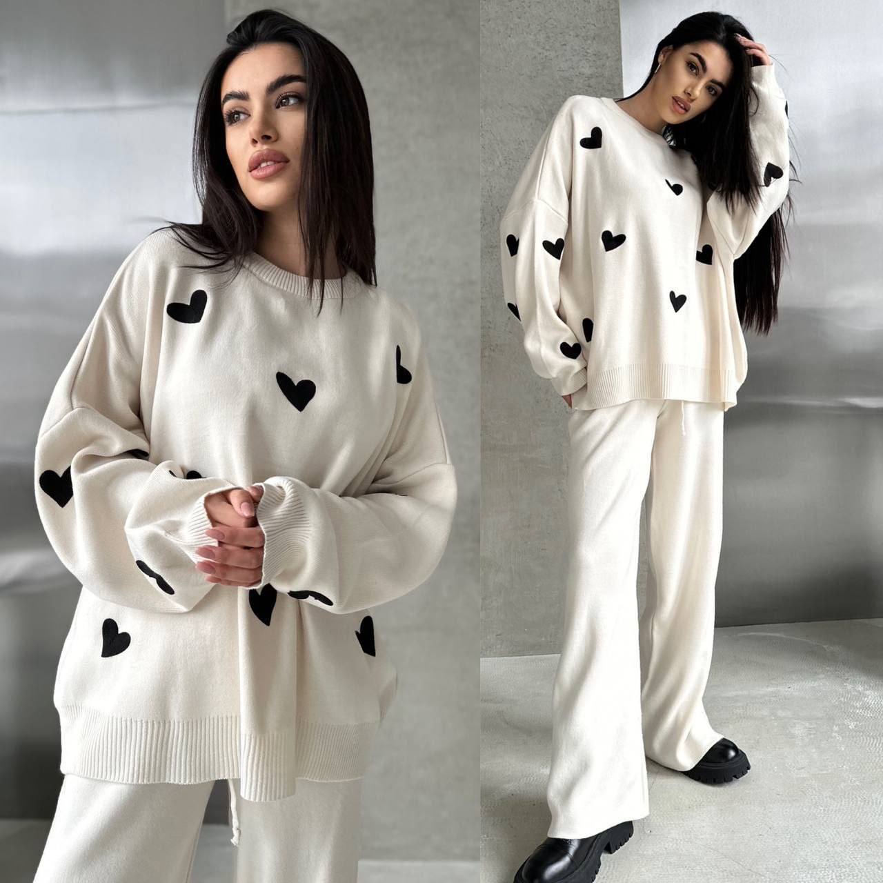 Woman wearing a white sweater and pants with black heart patterns against a gray background
