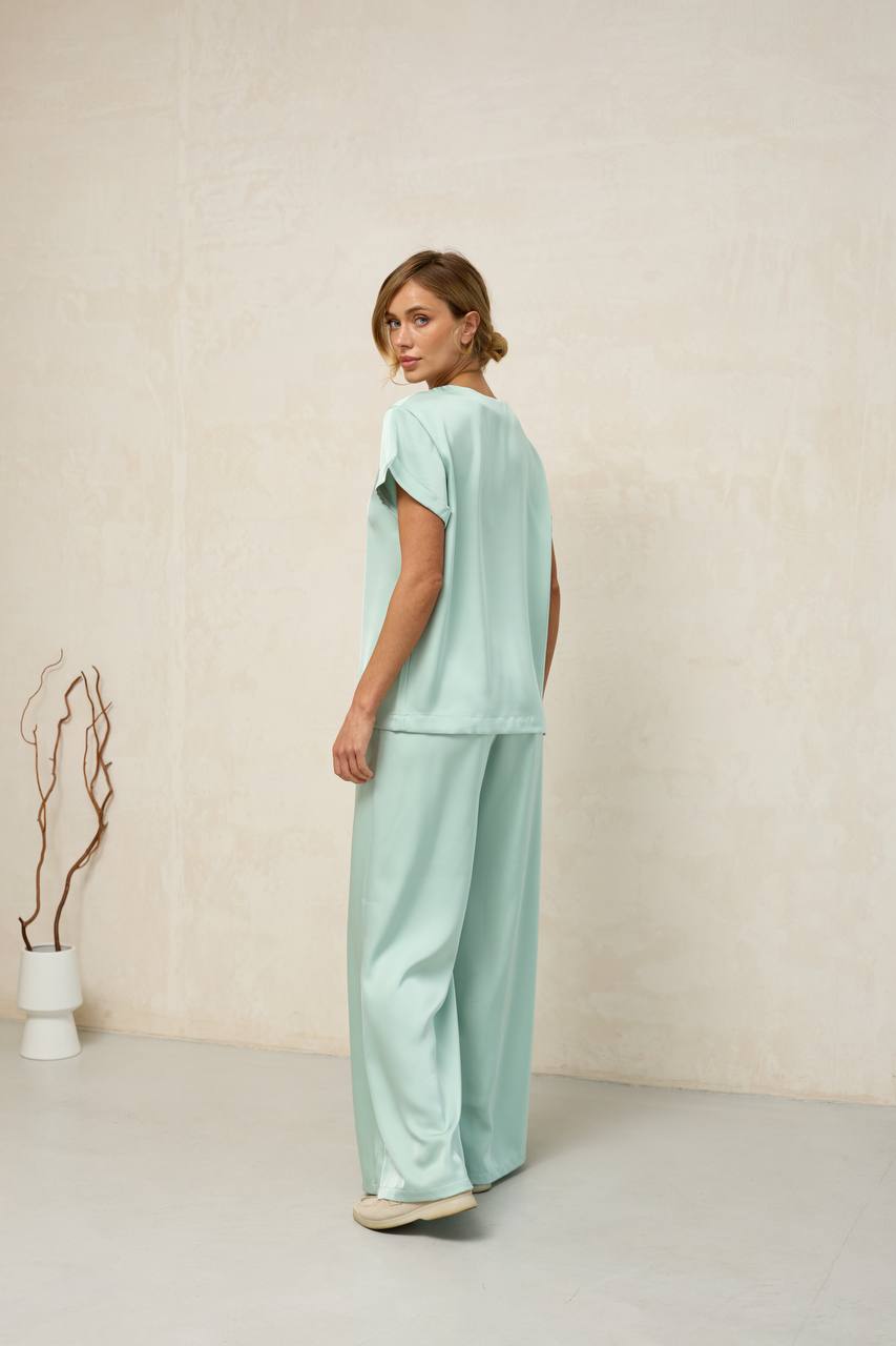 Woman wearing a light green outfit standing against a plain background