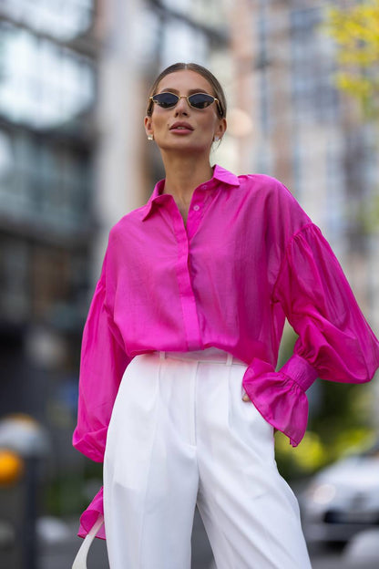 Woman wearing a bright pink shirt and white pants in an urban setting