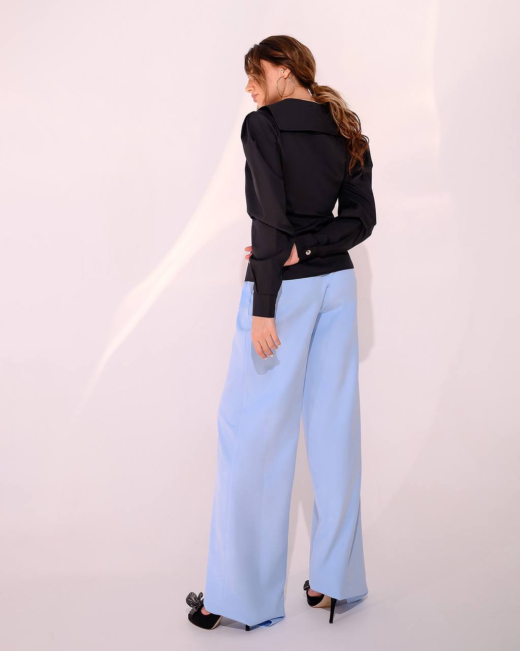 Person wearing a black jacket and light blue pants against a white background