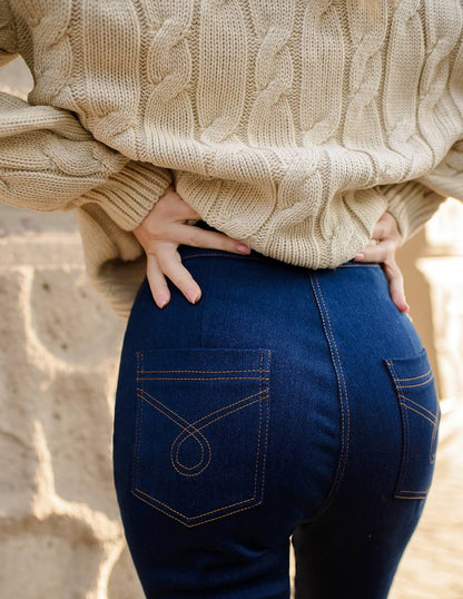 Person wearing a beige cable knit sweater and blue jeans with a blurred background