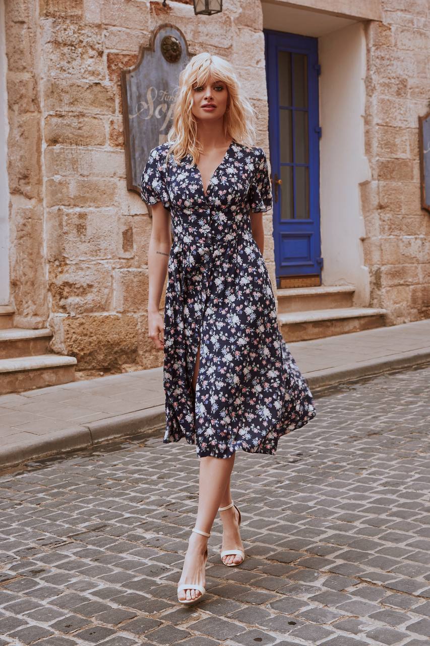 Woman in a floral dress standing on a cobblestone street in front of a building with a blue door.