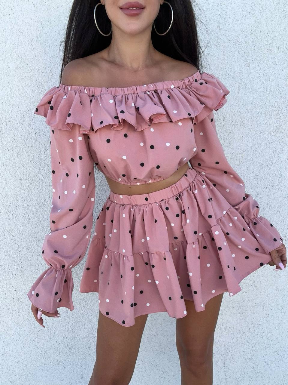 Woman wearing a pink polka dot off-shoulder top and skirt against a white background