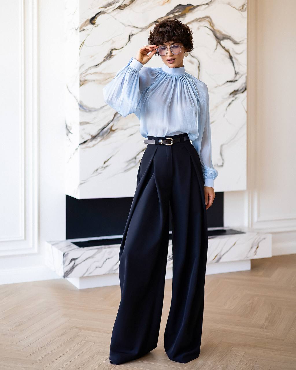 Person wearing a light blue blouse and dark navy wide-leg pants in an indoor setting.