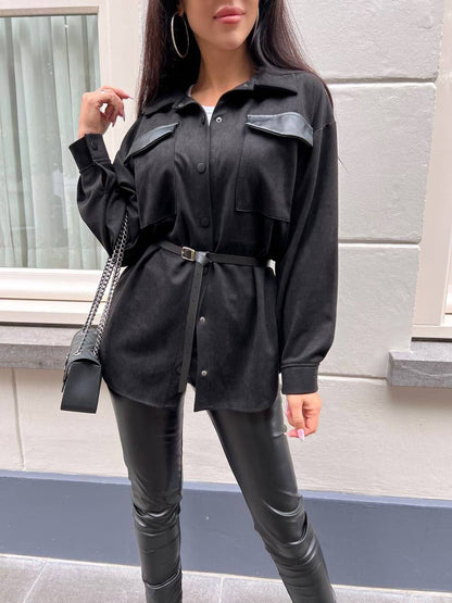 Person wearing a black outfit with leather pants standing against a light-colored wall.