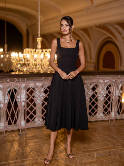 Woman in a black dress standing in an elegant indoor setting with chandeliers.