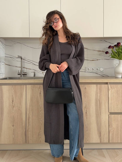 Woman in a long dark gray cardigan and jeans standing in a kitchen.
