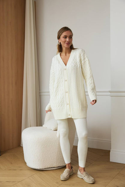Woman wearing a cream cardigan and pants standing in a room with wooden flooring and white walls.
