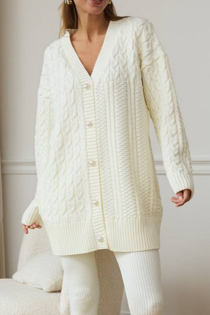 Woman wearing a long cream cable knit cardigan against a neutral background