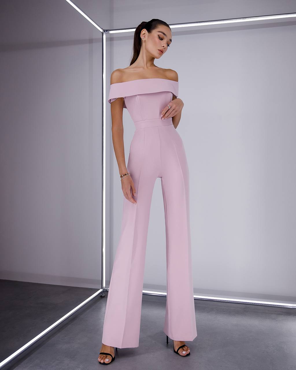 Woman wearing a pink off-shoulder jumpsuit in a minimalistic setting