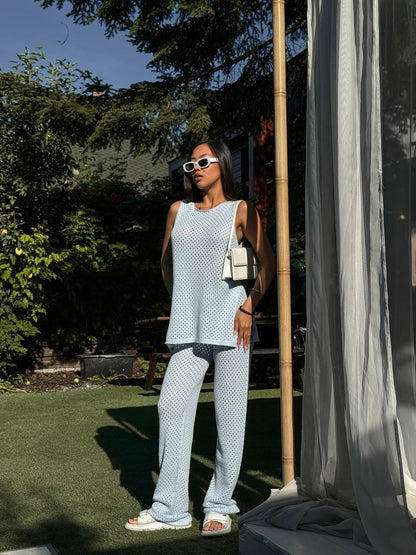 Woman in light blue polka dot outfit standing outdoors with greenery and a bamboo pole in the background.