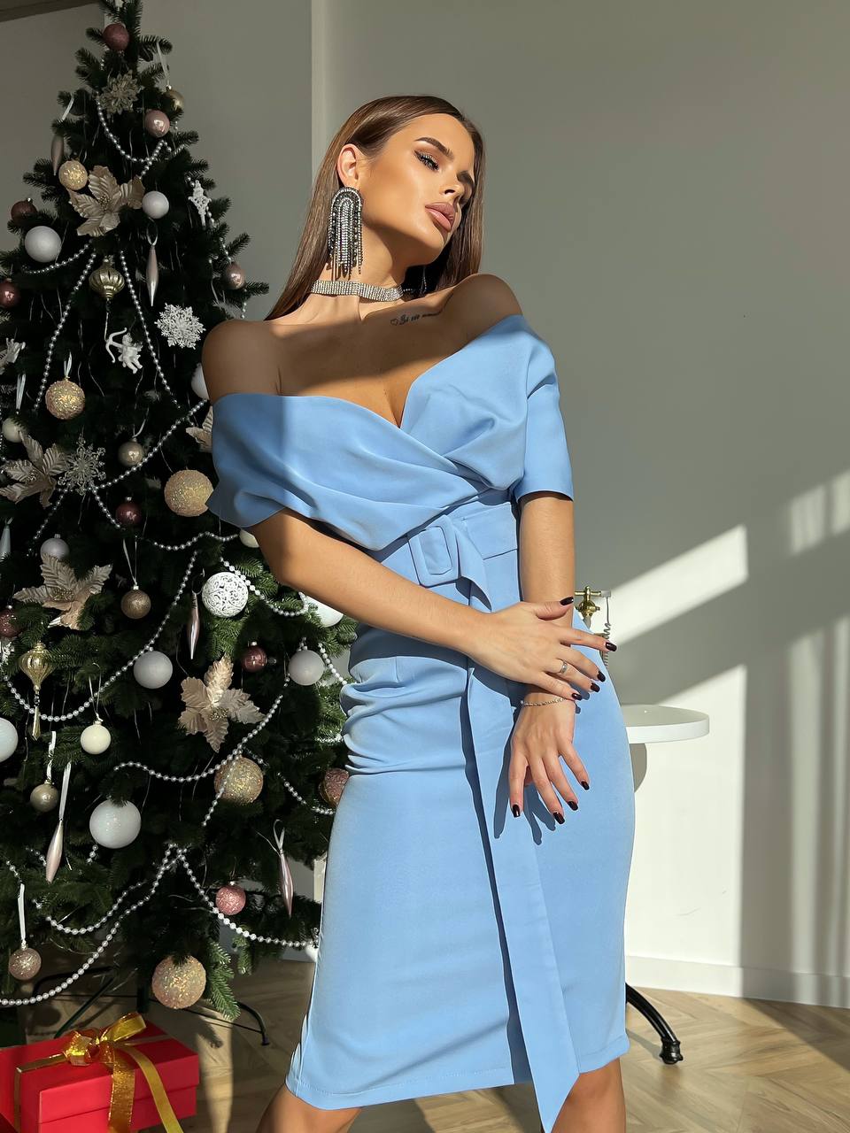 Woman in a blue dress standing next to a decorated Christmas tree indoors.