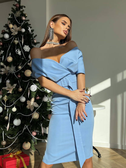 Woman in a blue dress standing next to a decorated Christmas tree indoors.