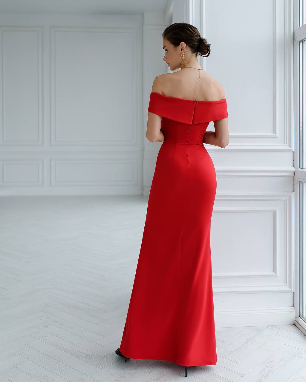 Woman wearing a red off-shoulder evening gown in a white room.