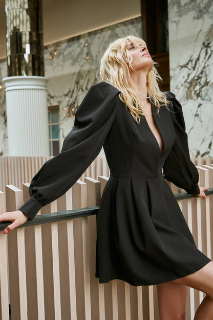 Woman in a black dress standing indoors with marble walls and wooden paneling.