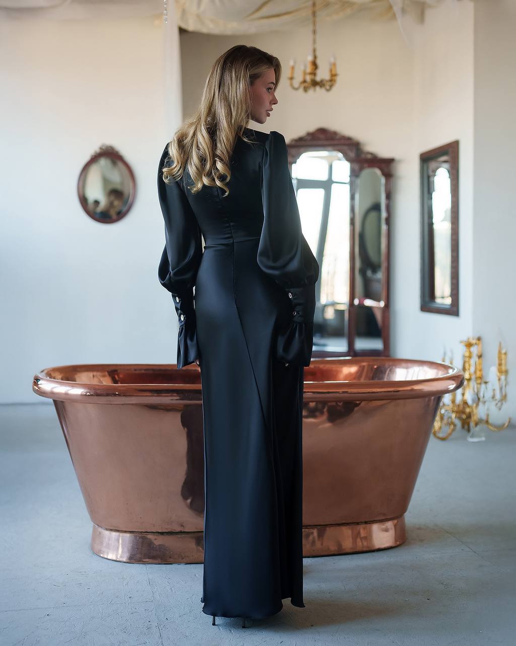 Woman in a black dress standing next to a copper bathtub in an elegant room.