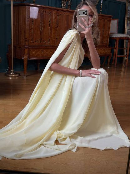 Woman in a flowing white dress sitting on a wooden floor in a room with wooden furniture.