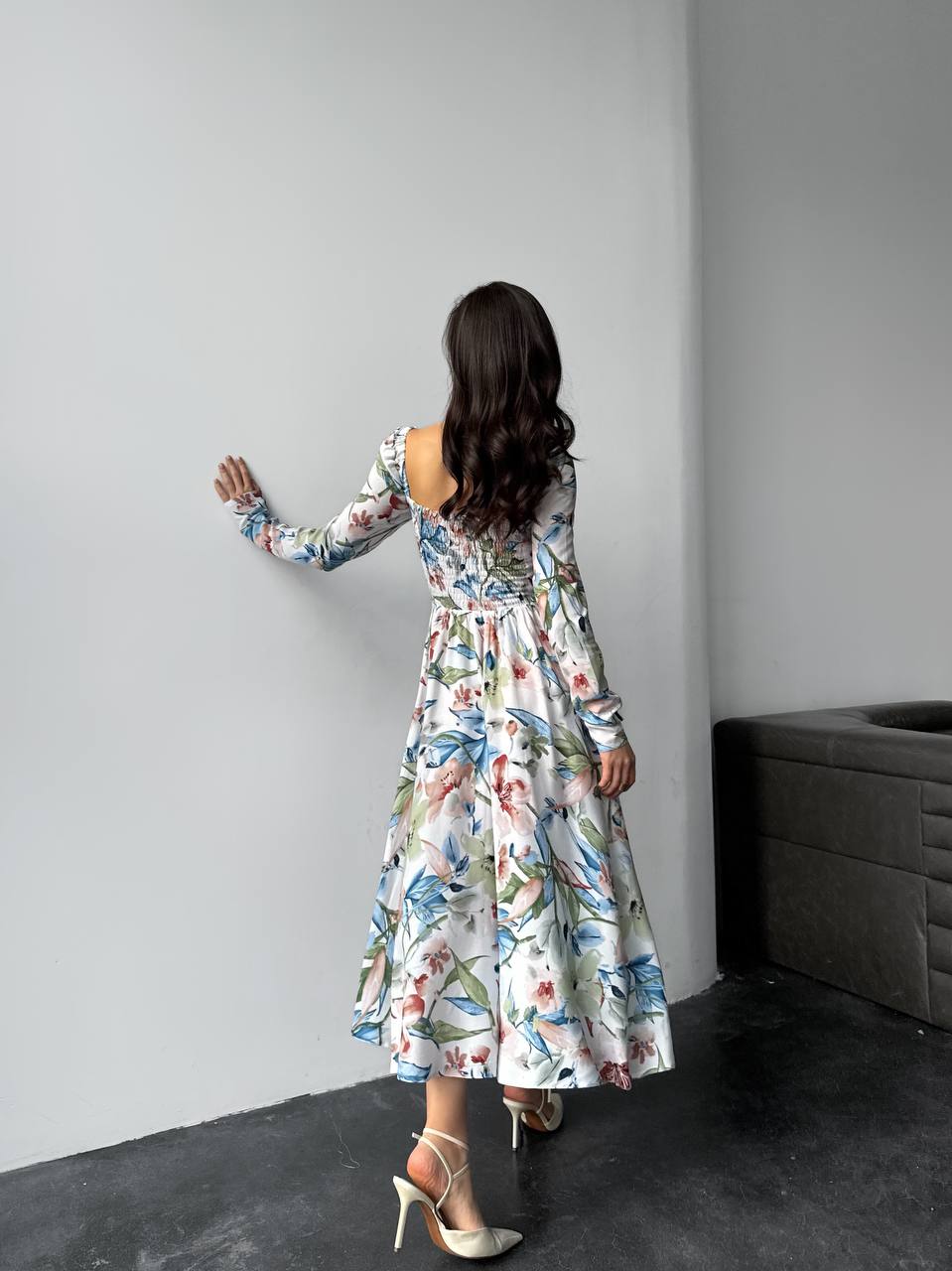 Woman in a floral dress standing against a gray wall