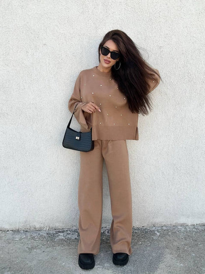 Woman in a brown outfit holding a black handbag against a white wall.