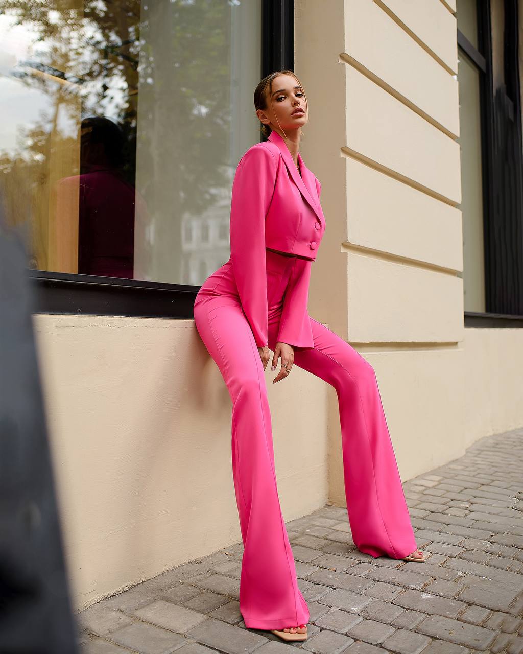Woman in a bright pink suit sitting on a building ledge.