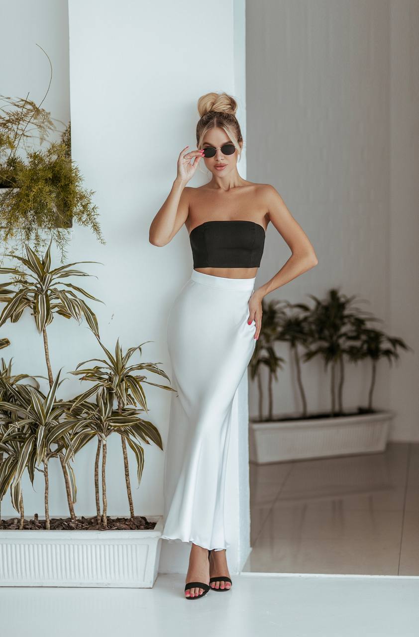 Woman in black top and white skirt standing indoors with plants in the background
