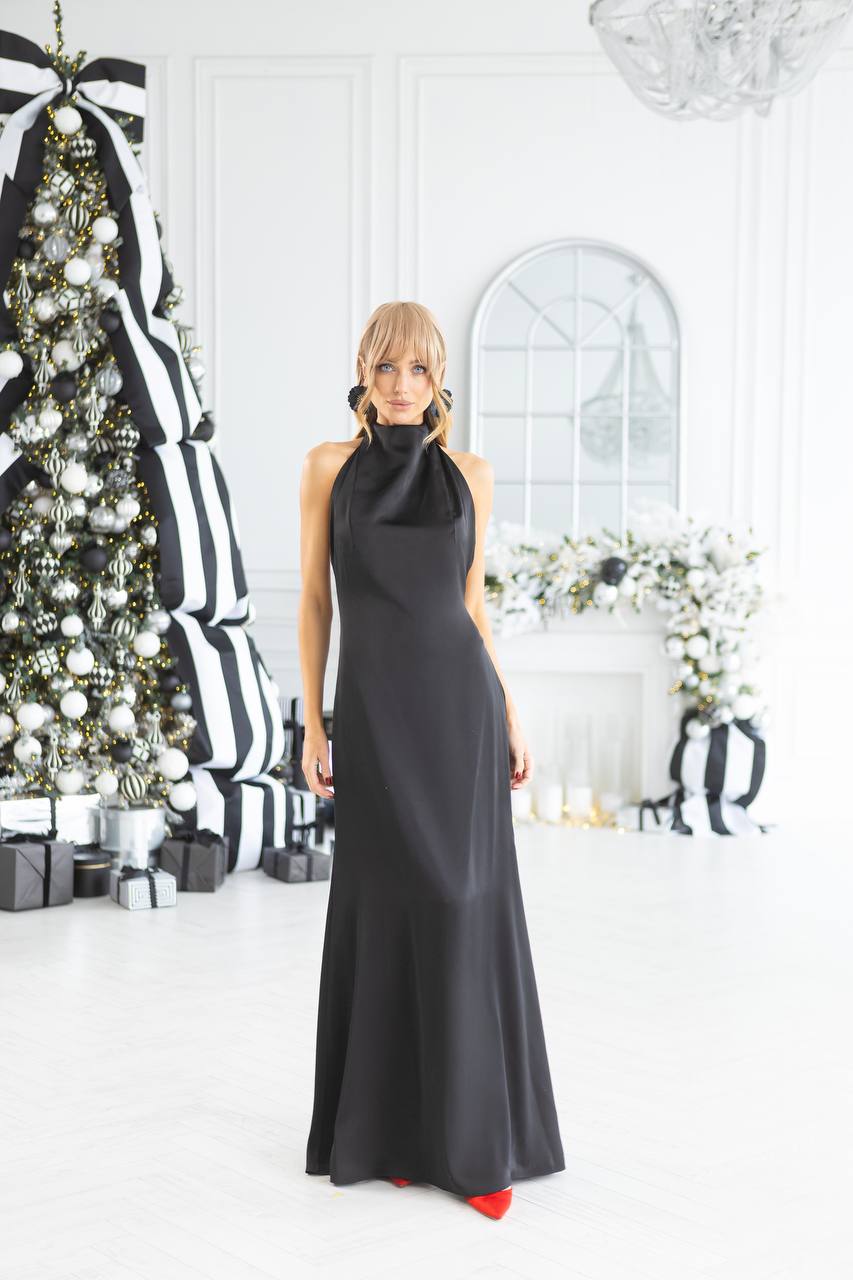 Woman in a black evening gown standing in a decorated room with Christmas tree and striped decorations.