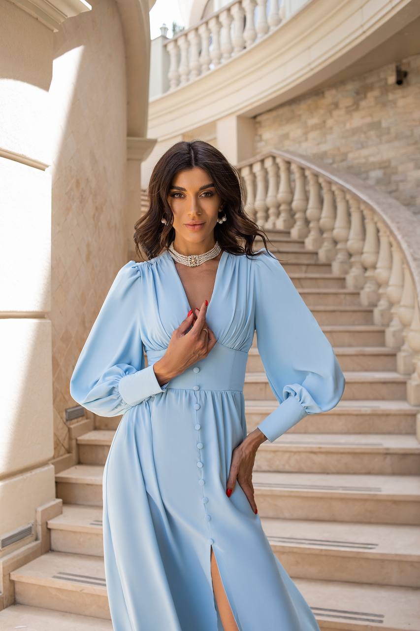 Woman in a light blue dress standing on a staircase with a classical design.