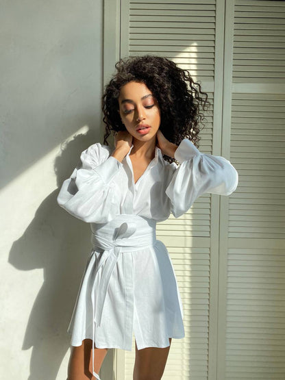 Woman wearing a white outfit standing against a light-colored wall.