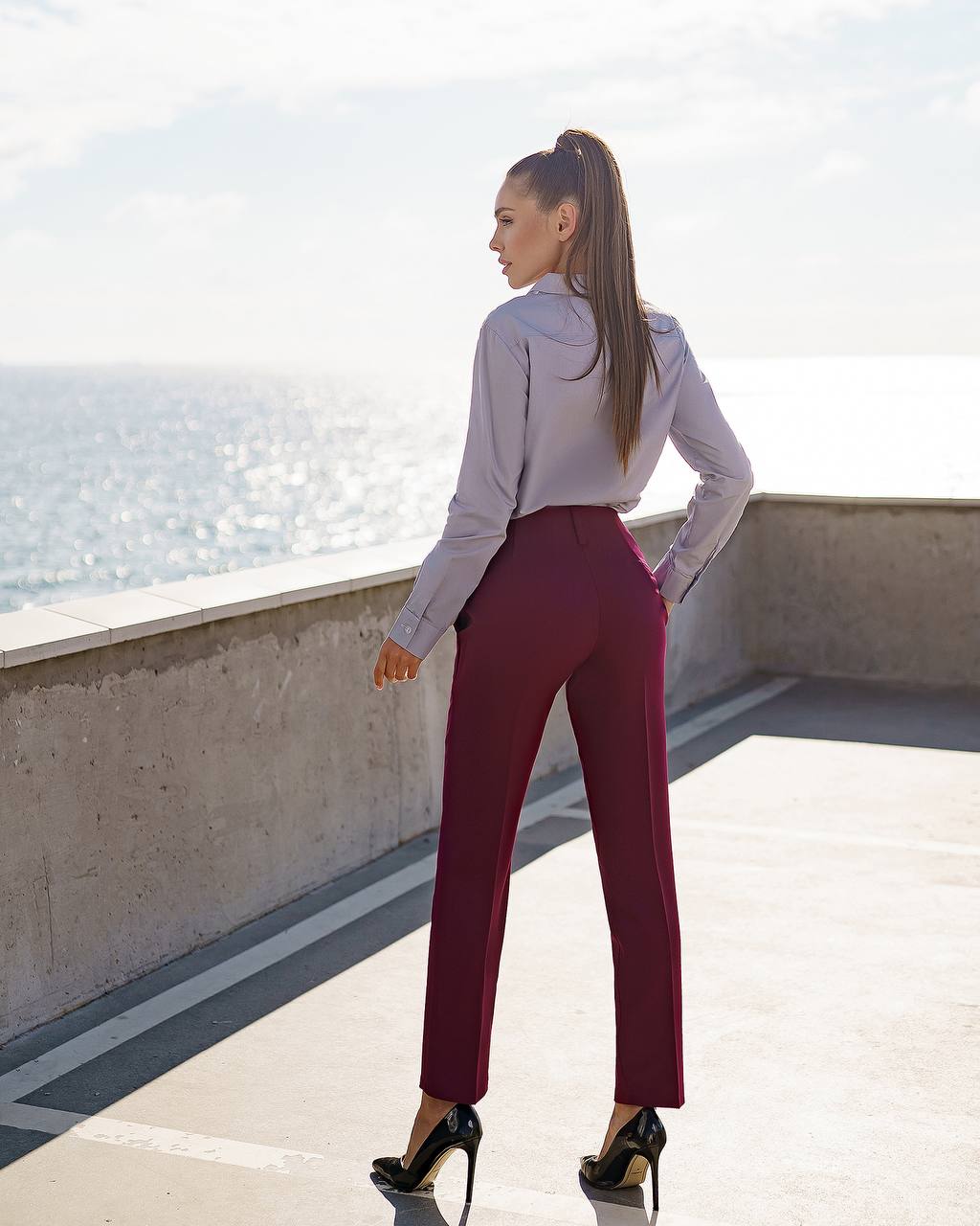 Woman in a white shirt and red pants standing on a rooftop with a scenic view.