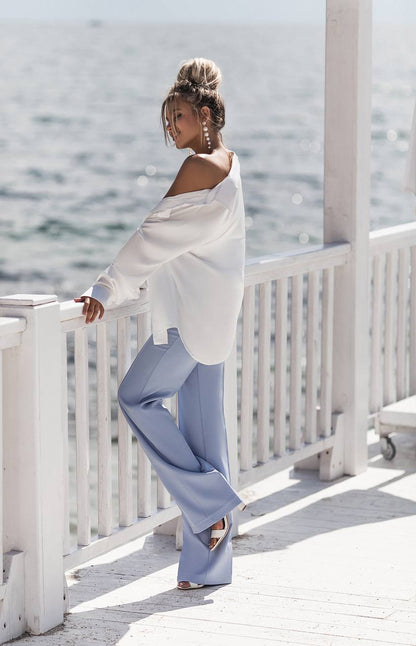 Woman in a white top and light blue pants standing on a white railing with water in the background