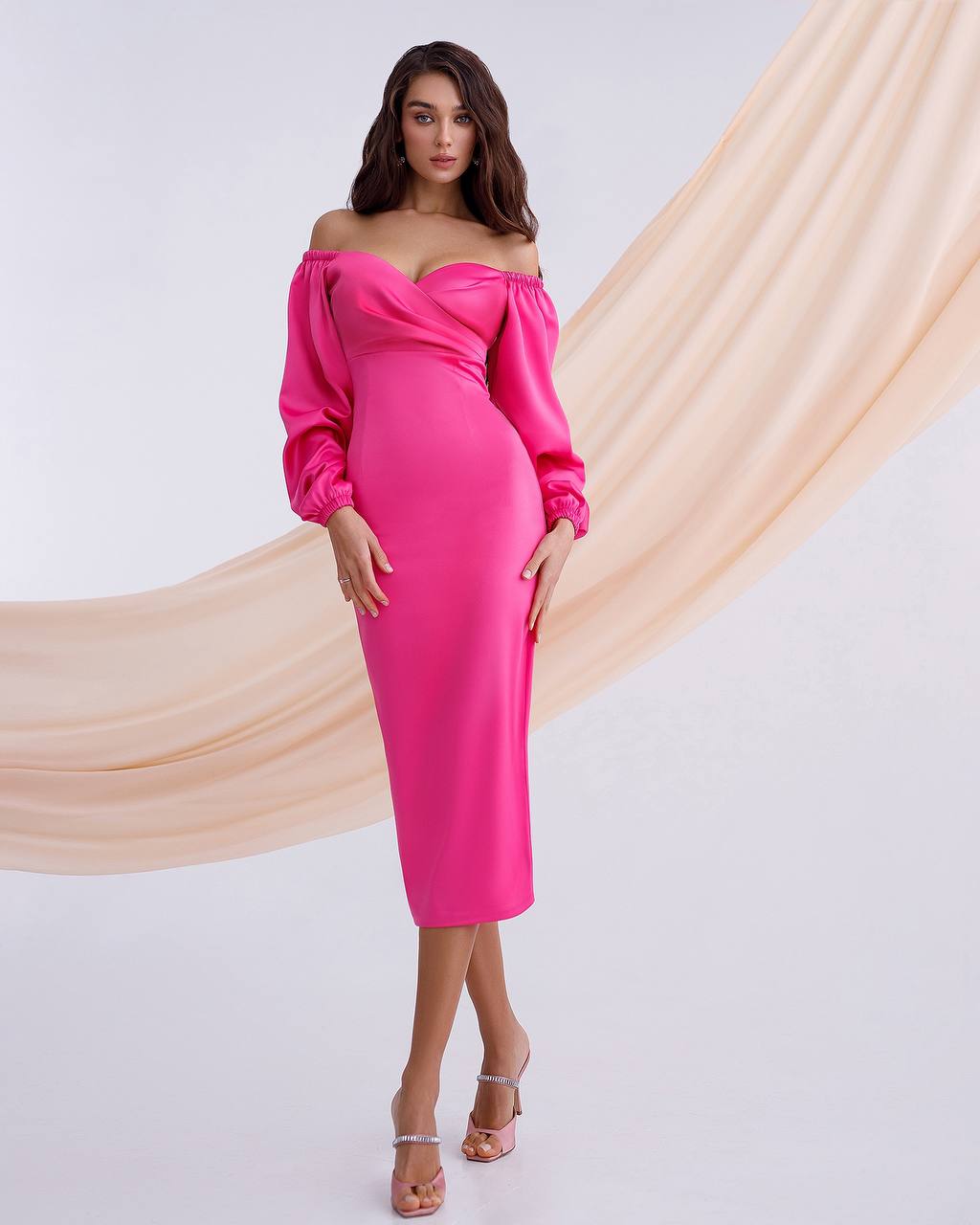 Woman wearing a bright pink off-shoulder dress with long sleeves against a beige curtain backdrop.