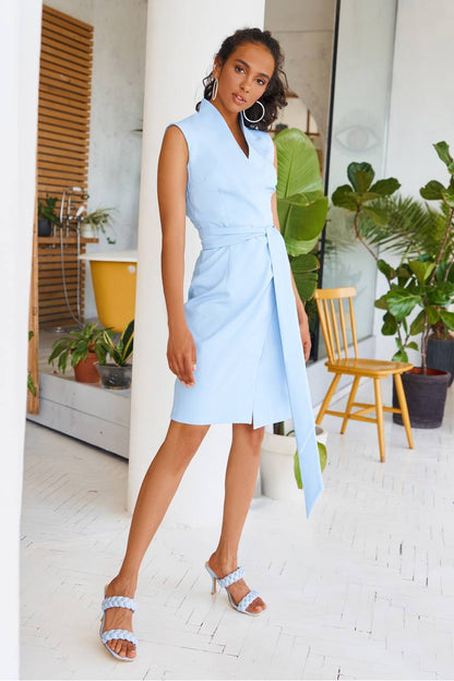 Woman in a light blue dress standing in a bright room with plants
