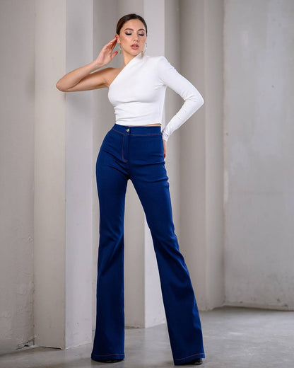 Woman wearing a white top and blue flared jeans against a plain background
