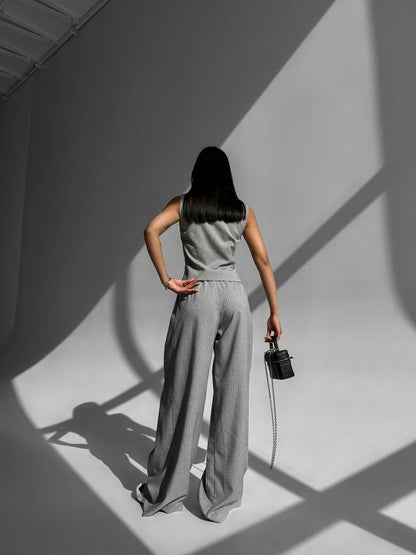 Woman in a gray jumpsuit standing in a studio with shadows on the floor