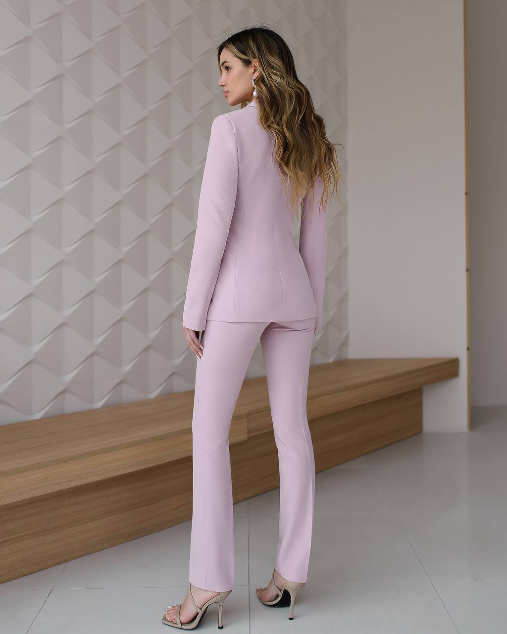 Woman in a light pink suit standing in a minimalistic room with geometric wall design.