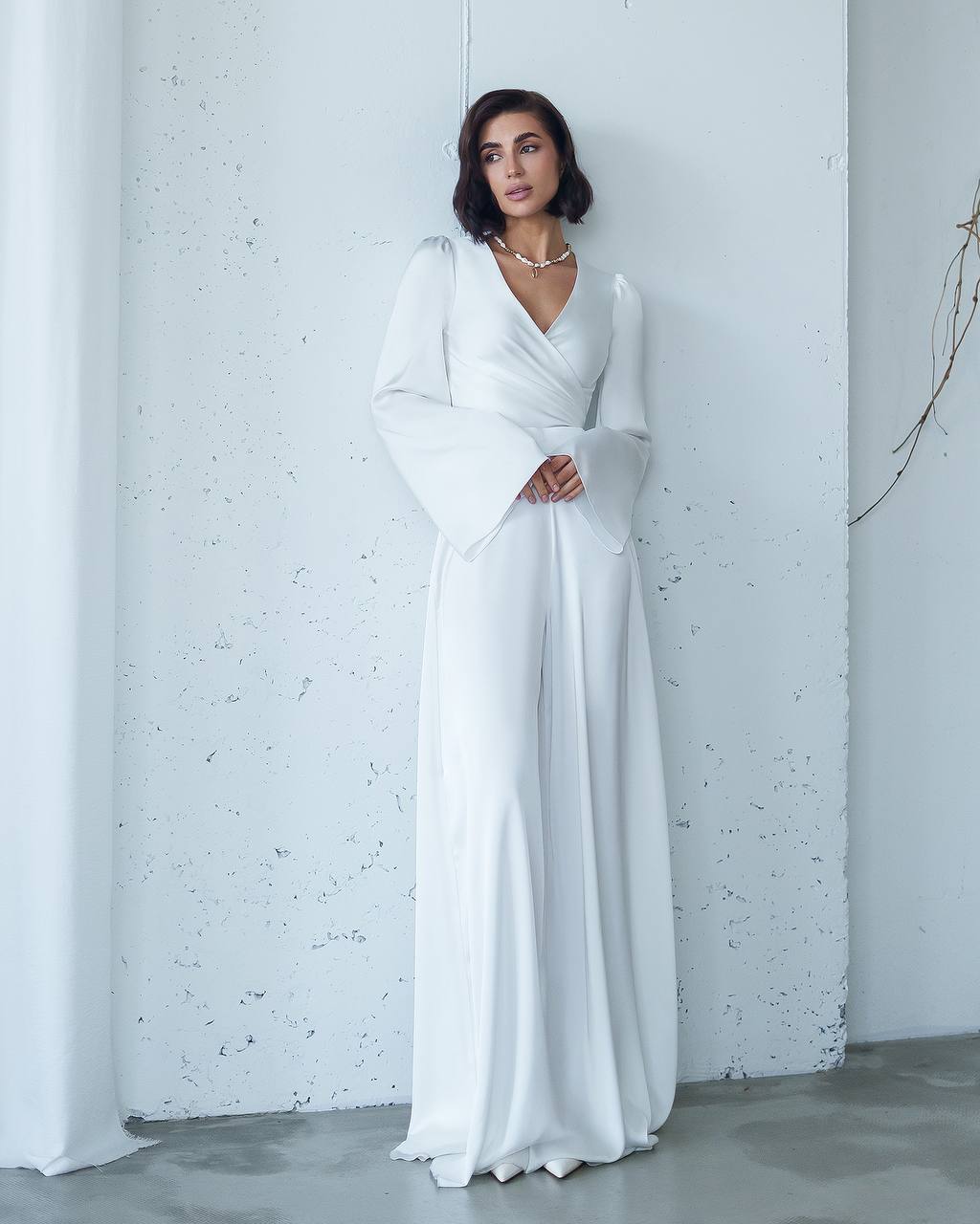 Woman wearing a white dress against a light gray wall.