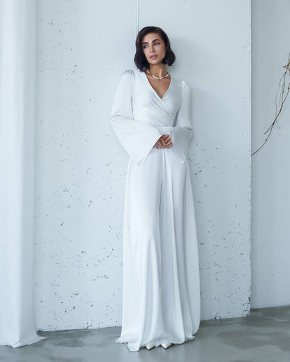 Woman wearing a white dress against a light gray wall.