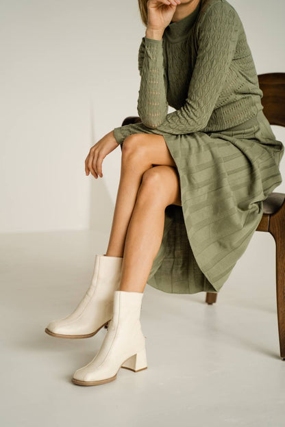 Person wearing a green dress and white boots sitting on a chair.