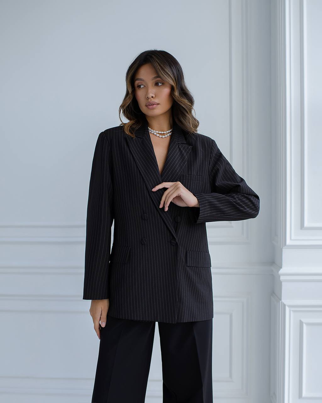 Woman wearing a black pinstripe suit against a white paneled wall