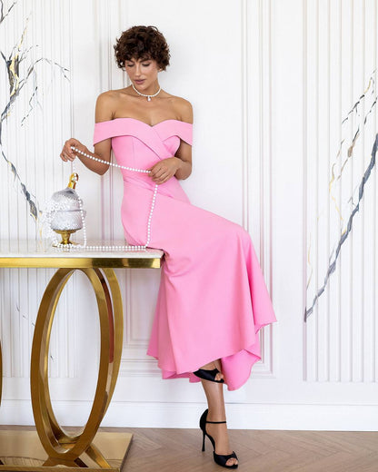 Woman in a pink off-shoulder dress sitting at a gold table with a white marble wall background