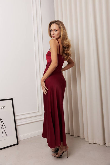 Woman in a burgundy dress standing in a room with white curtains and a framed picture on the wall.