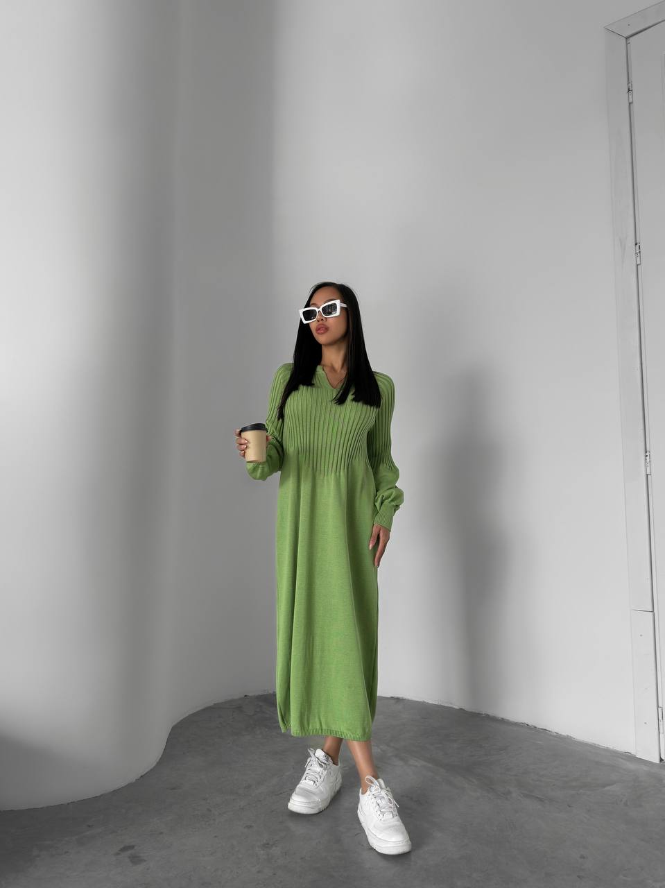 Woman in a green dress holding a coffee cup against a plain background