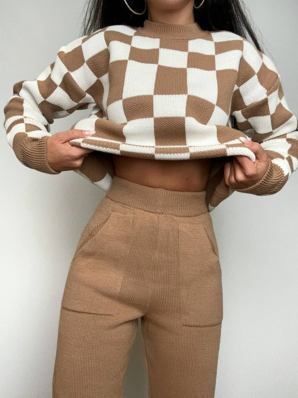 Person wearing a brown and white checkered sweater and matching pants against a plain background