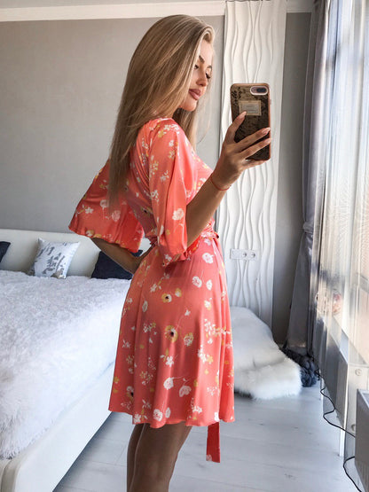 Woman in a floral pink dress taking a mirror selfie in a bedroom.
